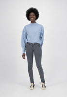 Person wearing a light blue sweater with puffed sleeves and fitted gray jeans, paired with black and white sneakers.