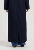 Dark blue denim trench coat shown from the back, styled over blue jeans and black heeled boots.