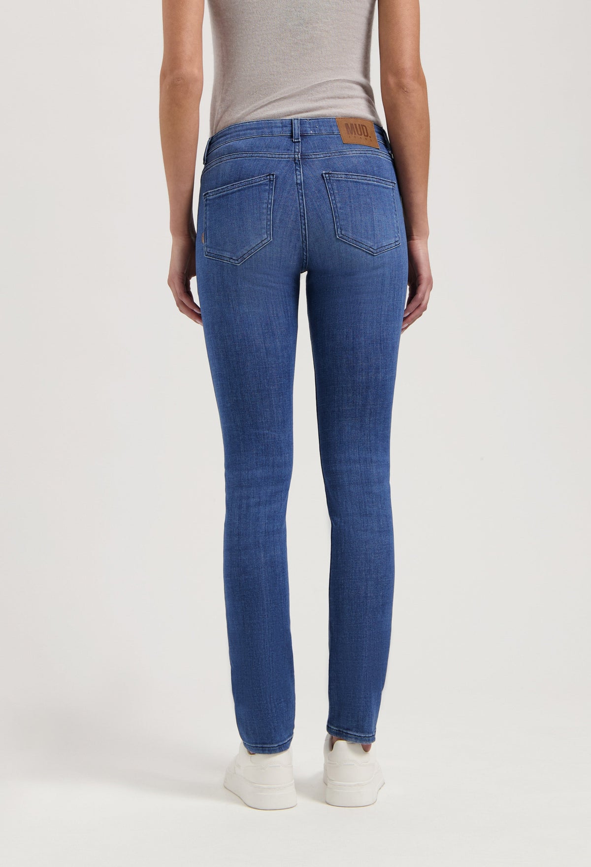 Back view of blue denim slim-fit jeans by MUD Jeans, made from organic cotton, paired with a light gray sleeveless top.