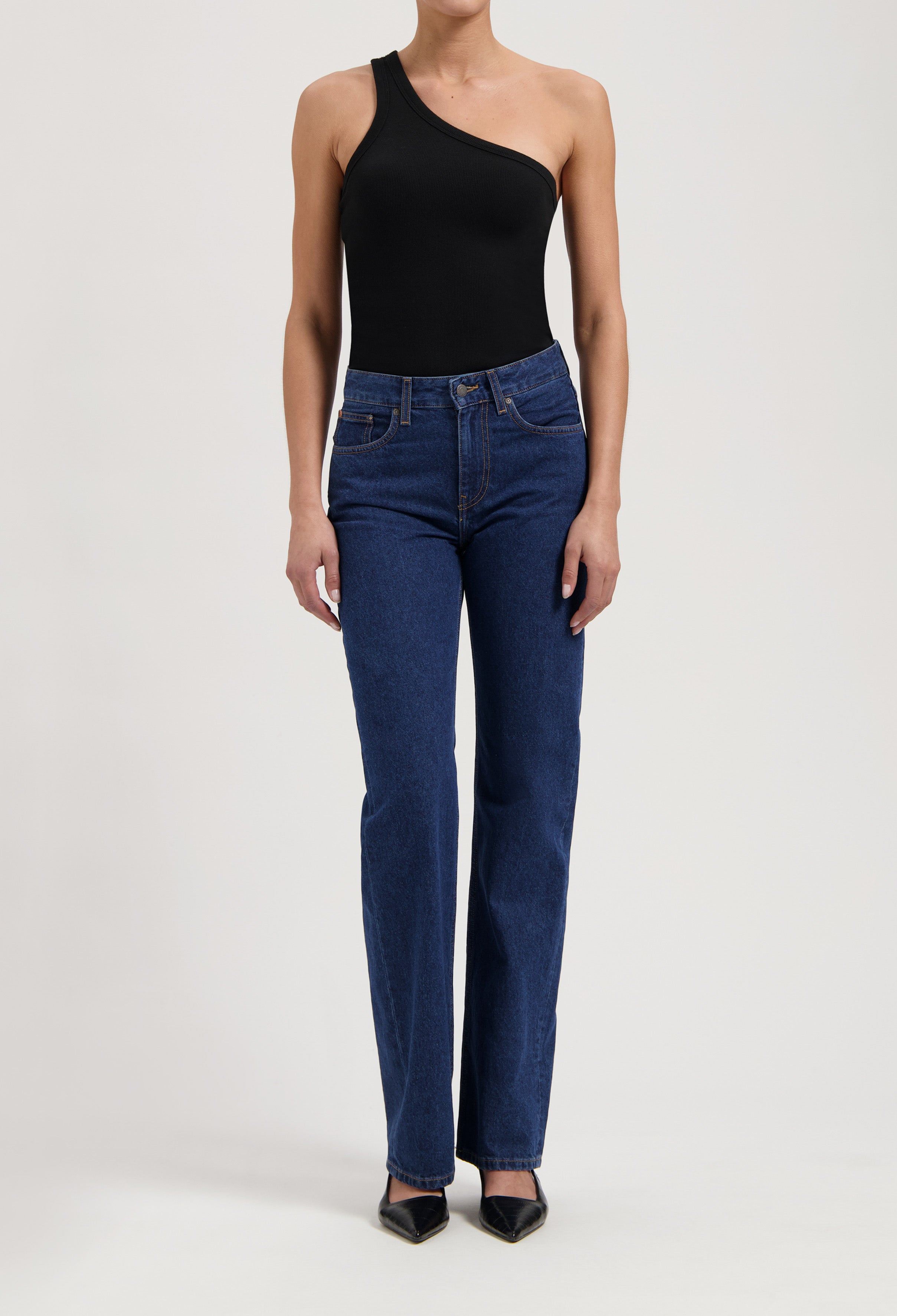 One-shoulder black bodysuit styled with classic dark blue high-waisted jeans and black pointed-toe heels.