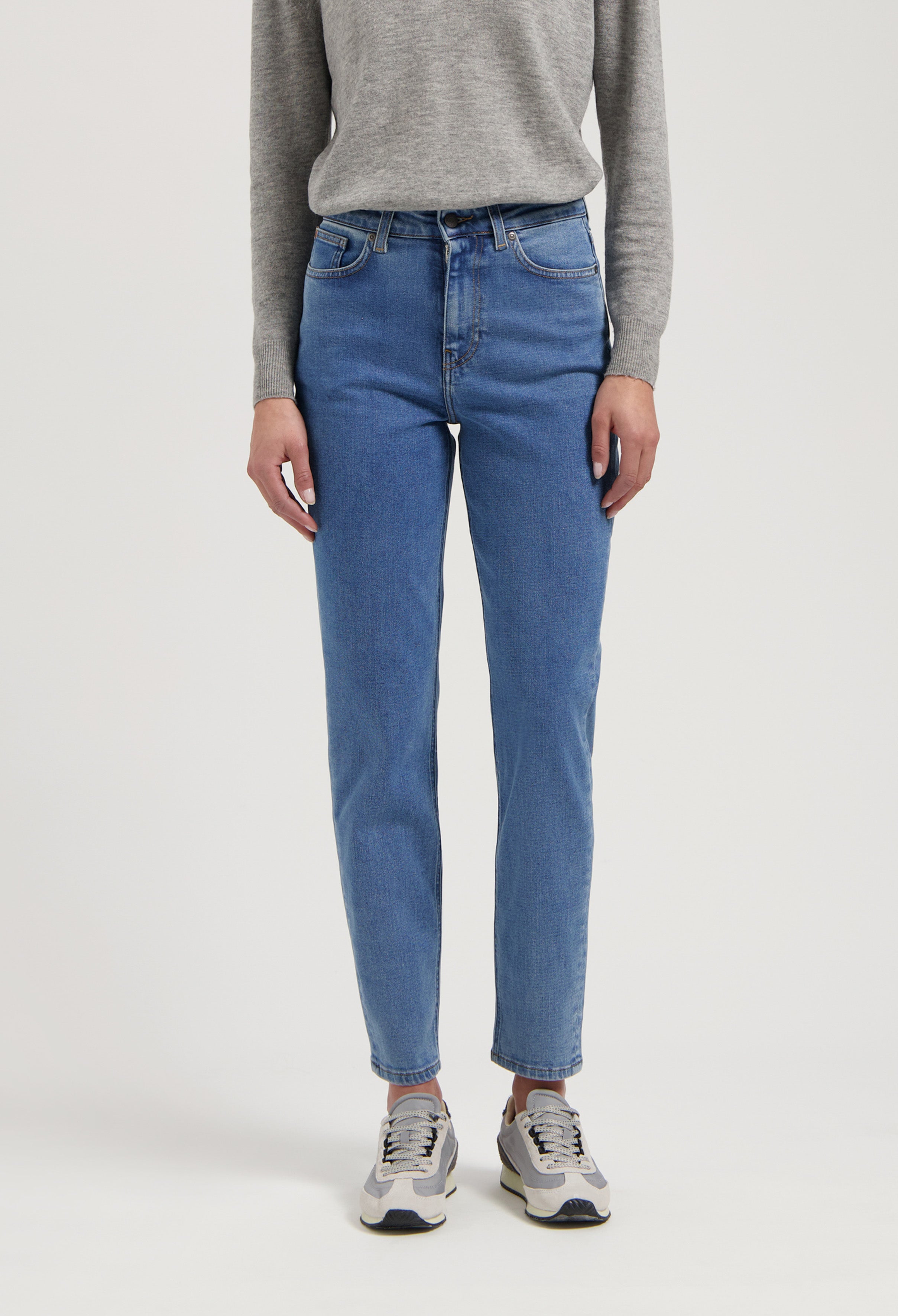 Gray long-sleeve top paired with light blue, high-waisted denim jeans and gray sneakers, showcasing casual everyday wear.
